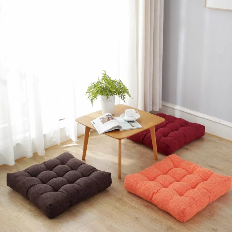 Grand coussin de sol carré en coton et lin, esprit tatami épais Nesty, trois coussins de sol carrés capitonnés unis, coloris brun, bordeaux et orange, posés au sol autour d'une table basse en bois