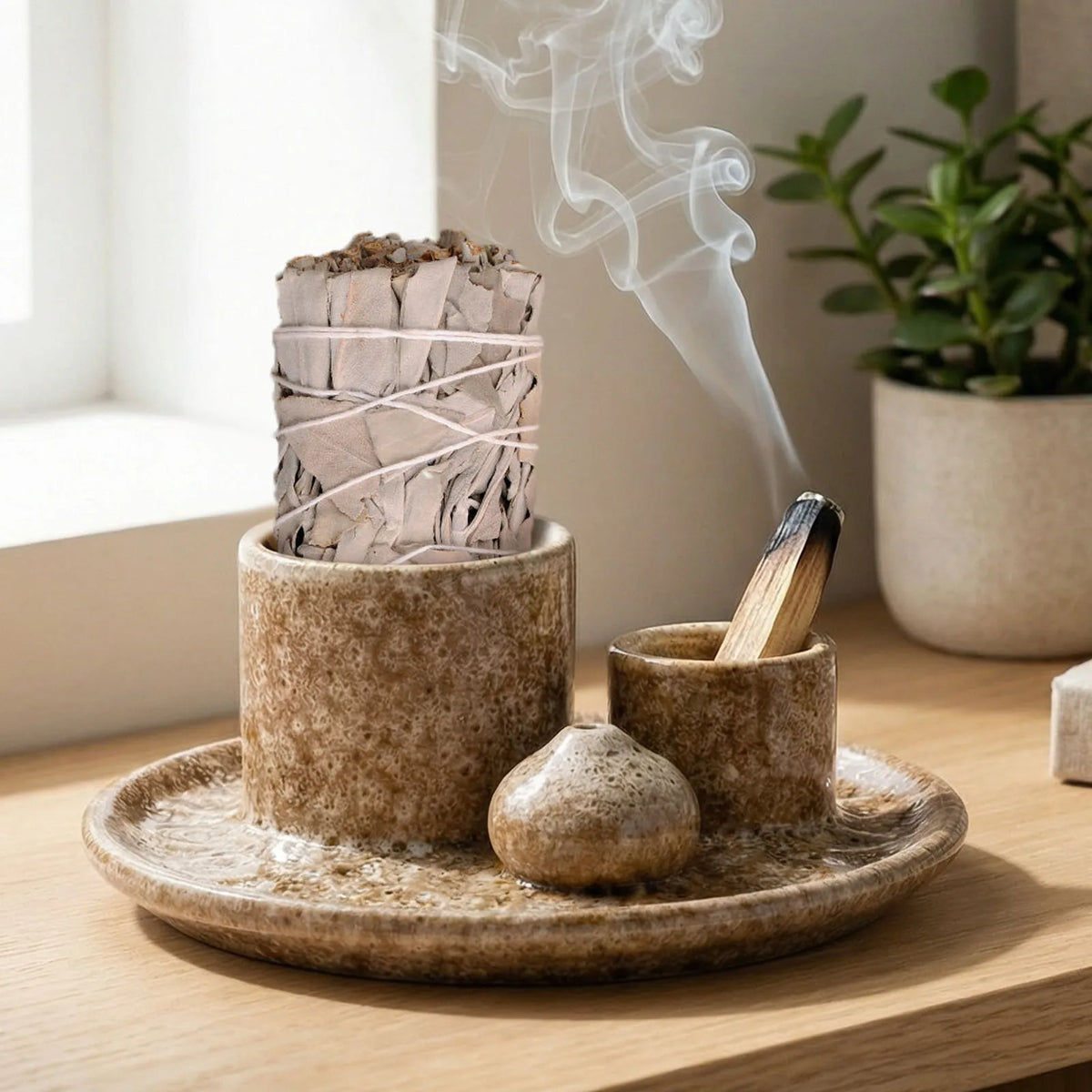Brûle-encens céramique 4-en-1 Nesty - Plateau avec bâton de sauge blanche fumant, bâtonnet d'encens, palo santo et pierre porte-encens, posé sur un rebord de fenêtre