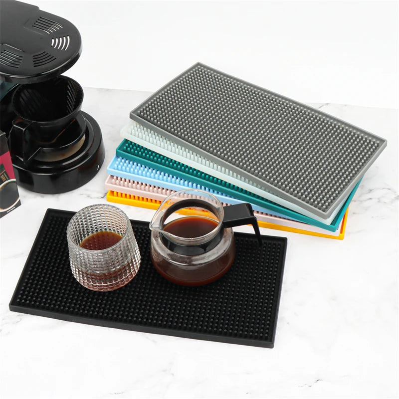 Tapis de bar en silicone gris avec verre et cafetière en verre remplis de café, pile de tapis colorés en arrière-plan - Nesty