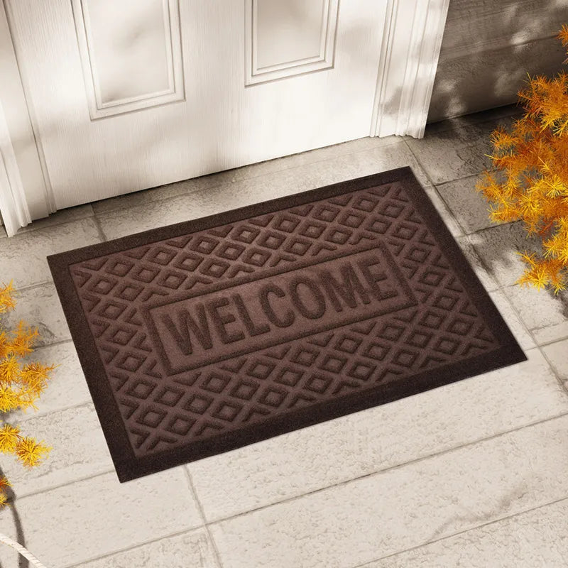 Paillasson en caoutchouc marron motif losanges gravé 'Welcome', posé devant une porte d'entrée blanche - Nesty
