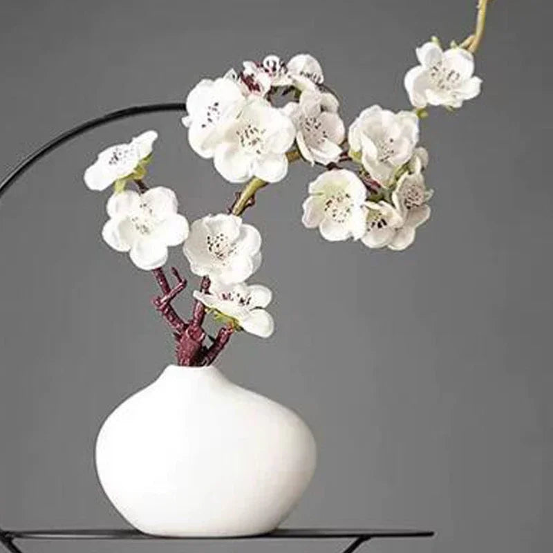 Vase en céramique blanche Nesty - Forme galet avec branche de fleurs de prunier blanches, sur support noir en arche, fond gris