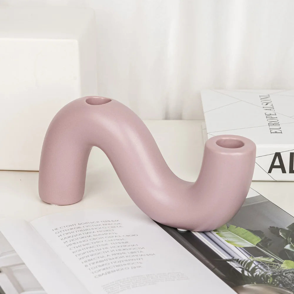 Bougeoir céramique rose poudré en forme de S ondulé à deux embouts, sur un livre ouvert - Nesty