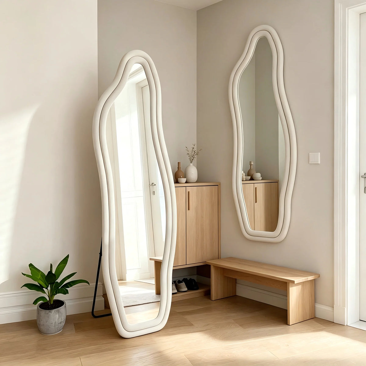 Grand miroir sur pied forme organique ondulée, cadre velours ivoire, dans une entrée avec plante verte et meuble en bois - Nesty