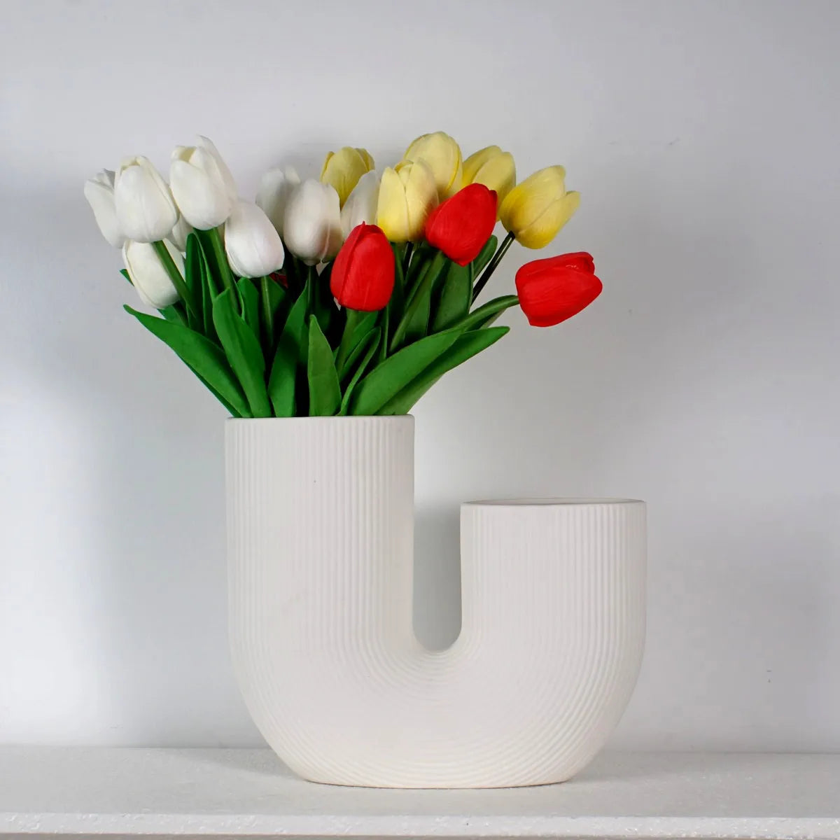 Vase céramique forme U, style nordique épuré - Nesty - Vase blanc en forme de U garni d'un bouquet de tulipes blanches, jaunes et rouges, sur une étagère