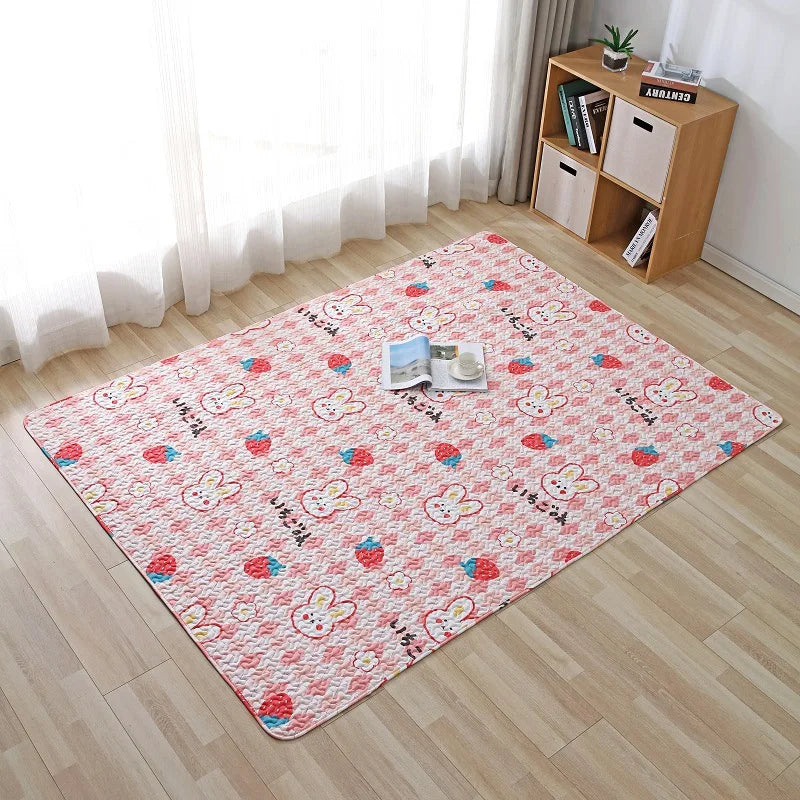 Tapis épais pour bébé — coin jeux - Nesty, tapis matelassé rose à motif lapins et fraises, sur parquet près d'une étagère avec magazine et tasse posés dessus