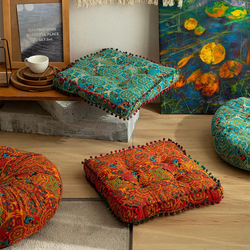 Gros coussin de sol en coton et lin épais, esprit marocain Nesty, coussins de sol carrés à pompons et motifs marocains bleu turquoise et orange, posés sur étagère et au sol près de tableaux