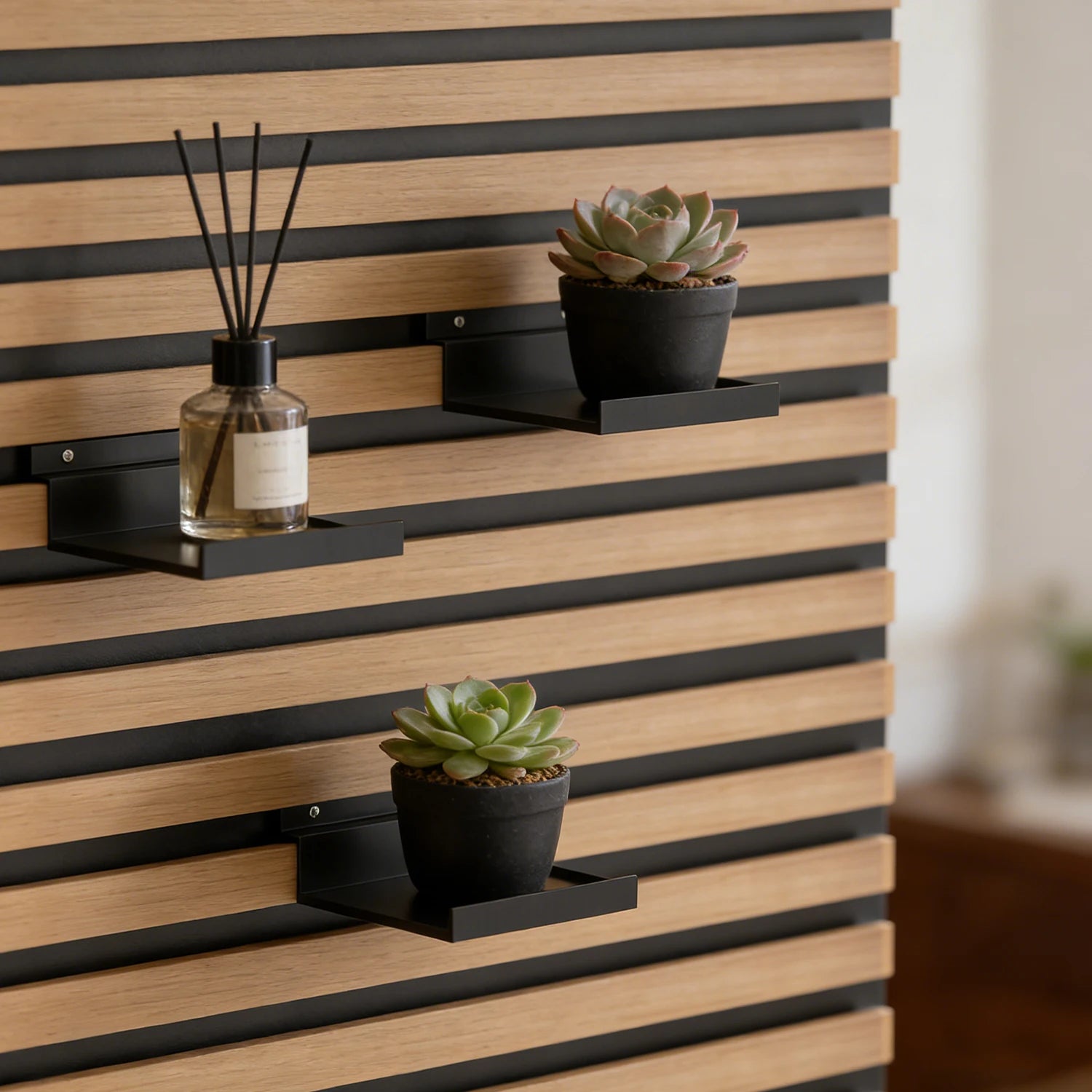 Étagère à clipser pour panneaux acoustiques Nesty, plusieurs étagères noires clipsées sur le panneau à lattes, diffuseur et plantes grasses en pot noir et blanc