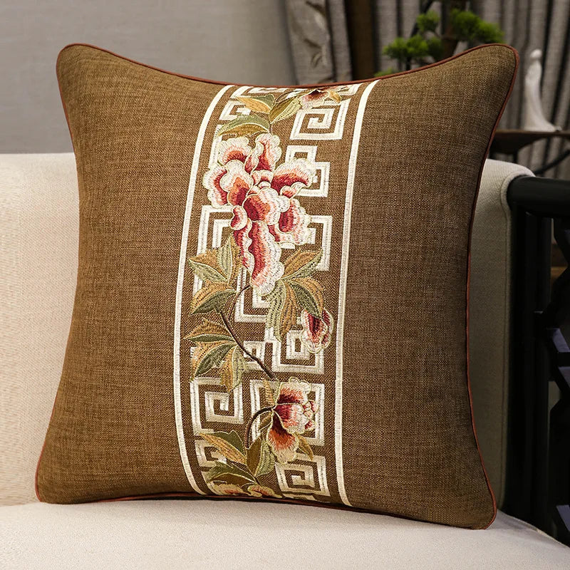 Housse de coussin en coton et lin, broderie florale classique Nesty, housse de coussin marron avec bande brodée de fleurs roses et motif grec ivoire, posée sur fauteuil