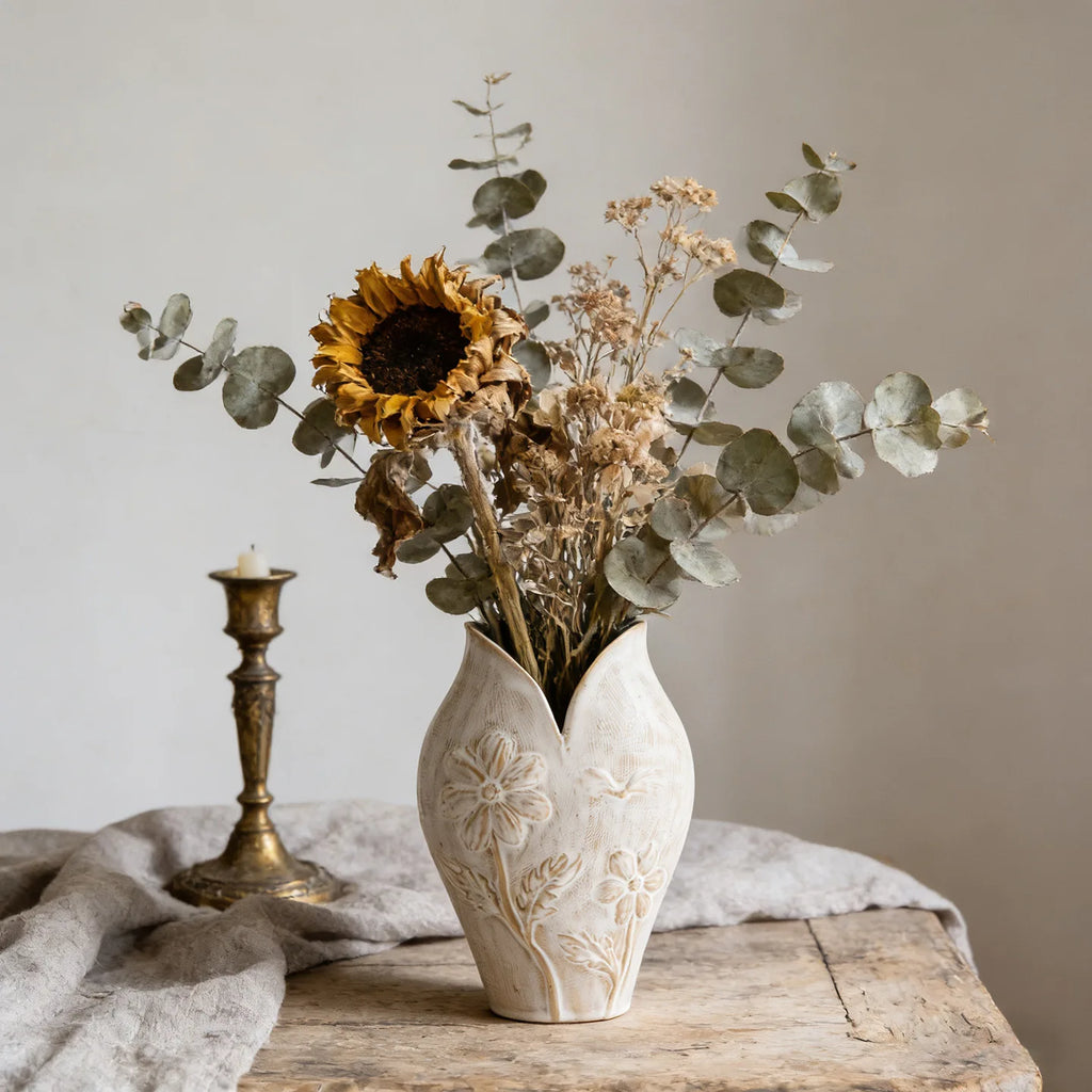 Vase en céramique forme poisson, esprit wabi-sabi Nesty, vase blanc à relief floral, garni d'un tournesol séché, eucalyptus et fleurs séchées, à côté d'un bougeoir en laiton