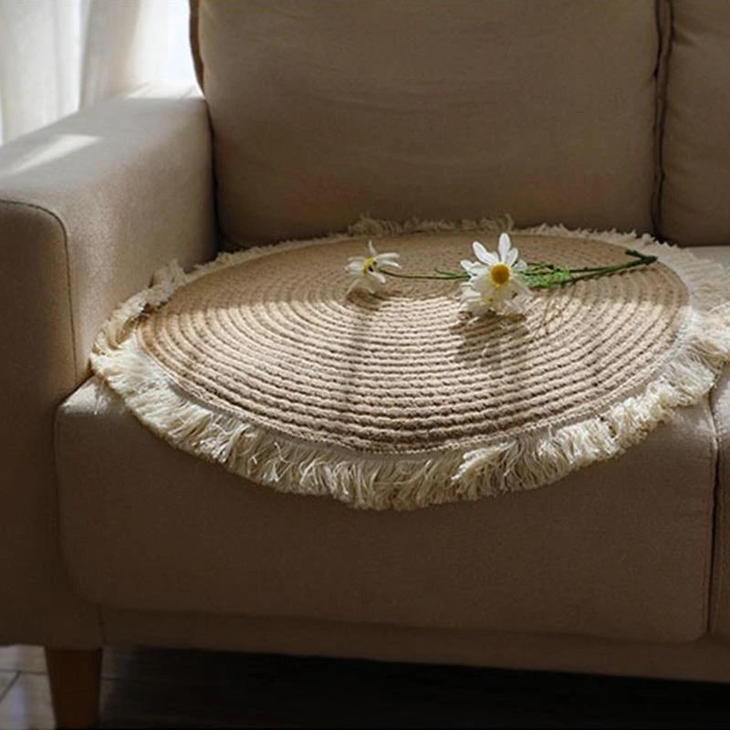 Petit tapis rond tissé à franges - Nesty, posé sur l'assise d'un canapé beige avec des marguerites