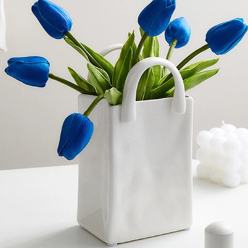 Vase blanc forme sac à main, fleurs séchées - Nesty - Grand modèle garni de tulipes bleues, posé sur une table blanche près d'une bougie ronde