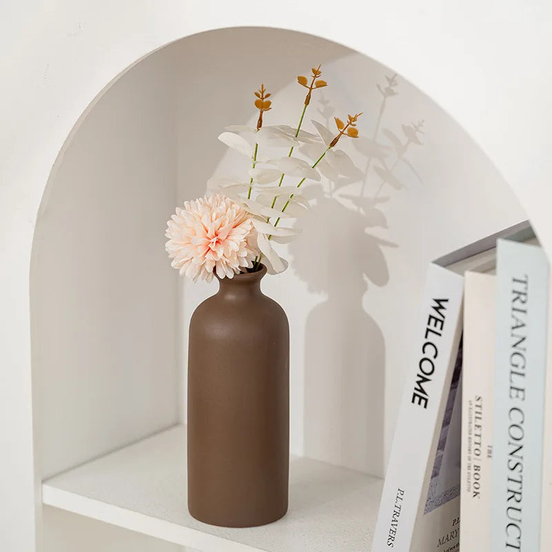 Vase en céramique blanc, style nordique minimaliste Nesty, vase cylindrique marron mat garni d'une fleur rose et de feuillage, dans une niche murale avec livres