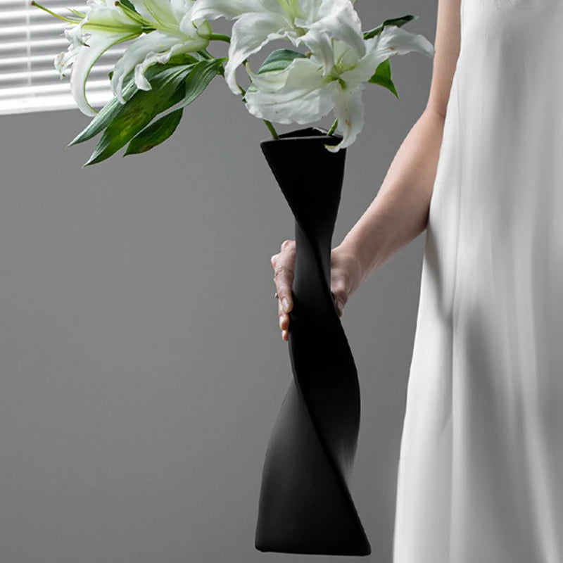 Vase céramique haut et torsadé Nesty - Coloris noir avec lys blancs, tenu à la main par une femme en robe blanche