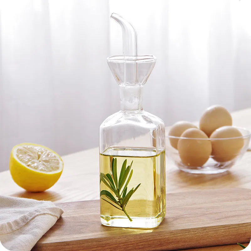 Pot à huile en verre borosilicate, anti-goutte Nesty, bouteille carrée avec brin de romarin dans l'huile, citron et bol d'œufs en arrière-plan