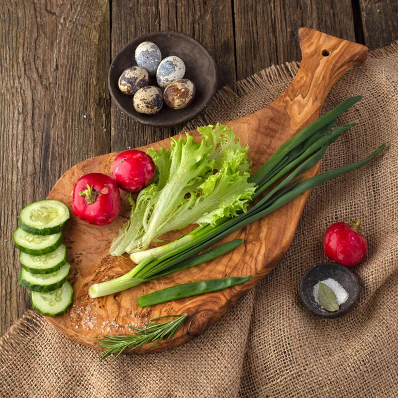 Planche à découper en bois d'olivier, forme irrégulière Nesty, planche irrégulière garnie de radis, salade, oignons nouveaux, concombre en tranches et œufs de caille