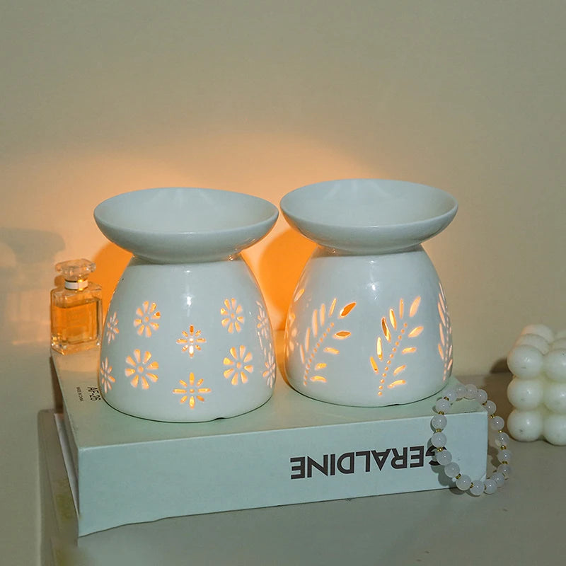 Brûle-parfum en céramique ajourée Nesty - Deux modèles blancs à motifs fleurs et feuilles, allumés côte à côte