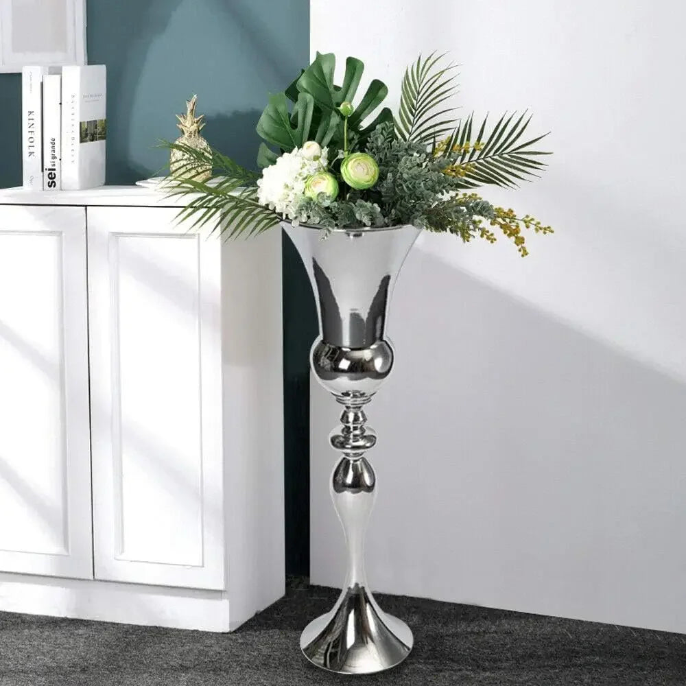 Grand vase sol en métal argenté Nesty - Avec feuillage tropical et fleurs blanches et vertes, près d'un meuble blanc et de livres