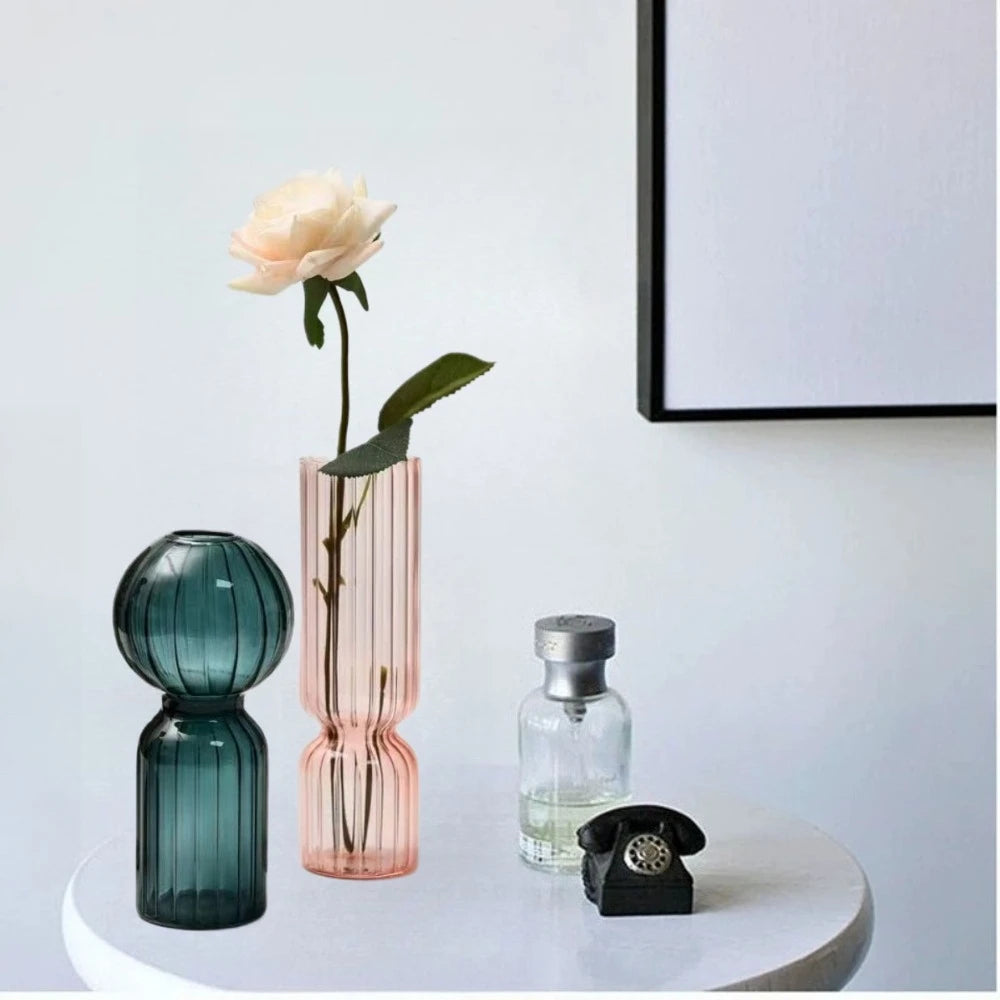 Vase en verre strié coloré, esprit scandinave Nesty, vase bleu canard forme boule et vase rose garni d'une rose, sur console avec flacon et téléphone miniature
