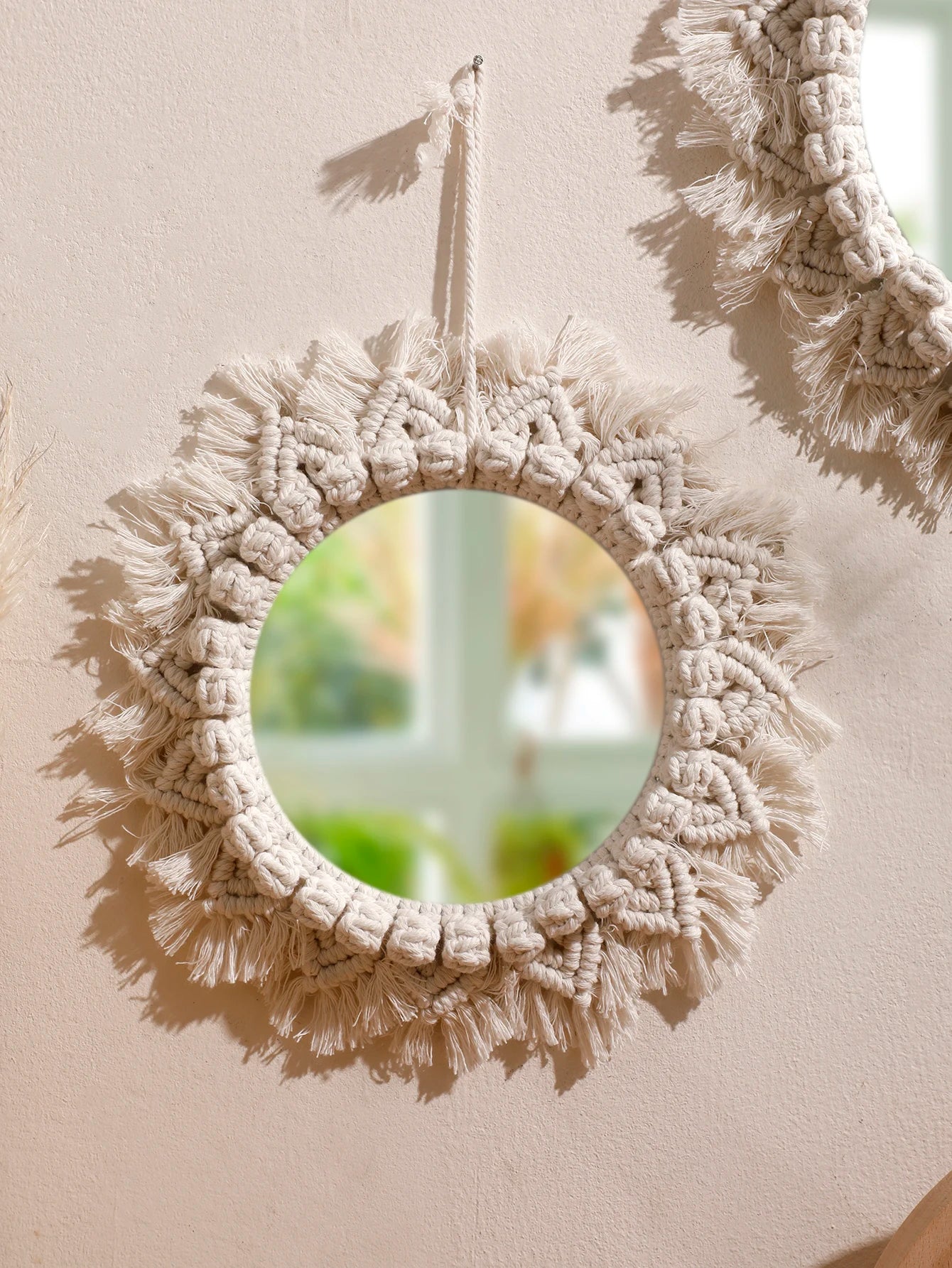 Miroir mural rond macramé à franges suspendu, avec un second miroir en arrière-plan, contre un mur beige - Nesty