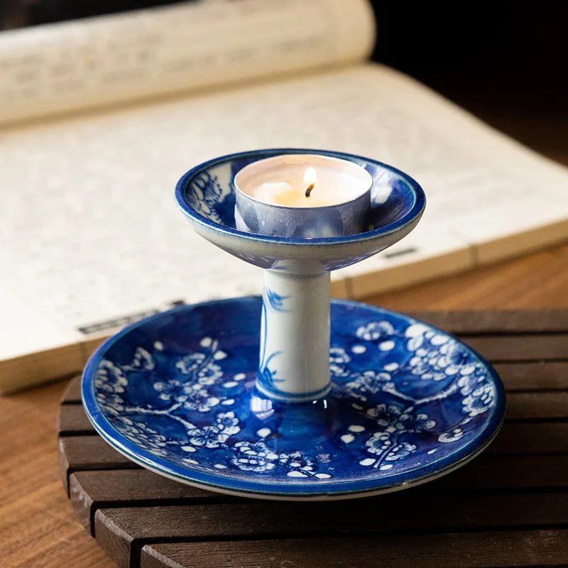 Bougeoir en porcelaine peinte à la main bleu motif fleurs de prunier, bougie chauffe-plat allumée, sur table en bois avec livre - Nesty