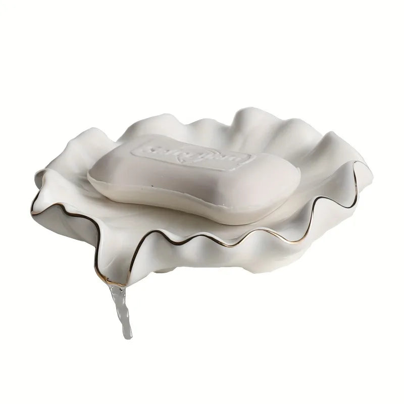 Porte-savon en céramique blanche forme coquillage à liseré doré avec savon, eau s'écoulant du rebord, sur fond blanc - Nesty