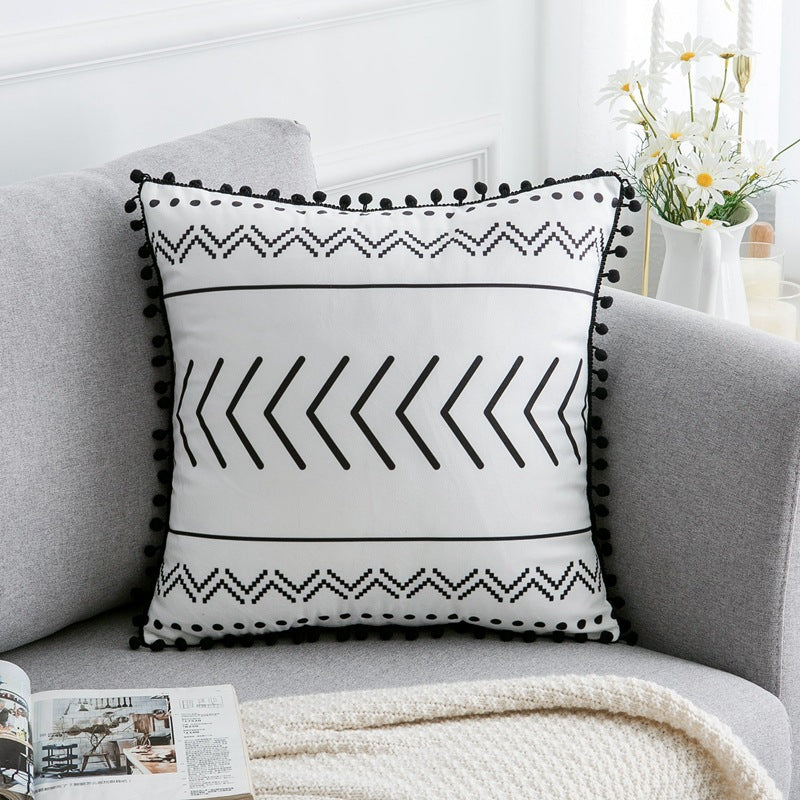 Housse de coussin en polyester satiné Nesty - Motif chevrons et zigzags noirs, bordure à pompons, sur un canapé gris