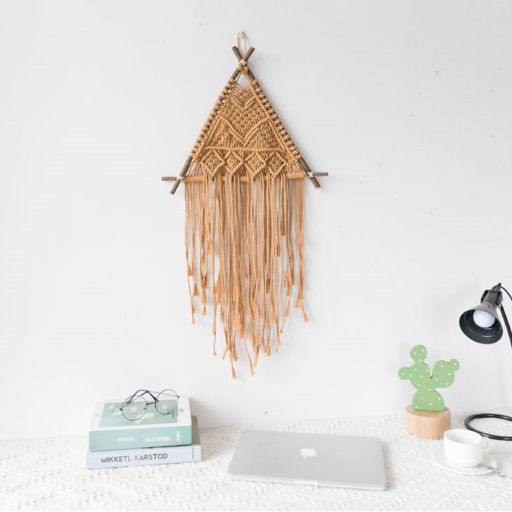 Suspension murale en macramé Nesty - Tenture triangulaire ocre sur mur blanc, au-dessus d'un bureau