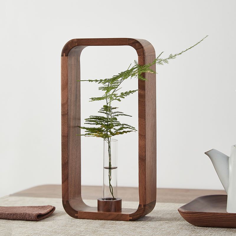 Vase soliflore en bois et verre Nesty - Cadre rectangulaire en noyer et tube en verre garni d'une fougère, sur une table